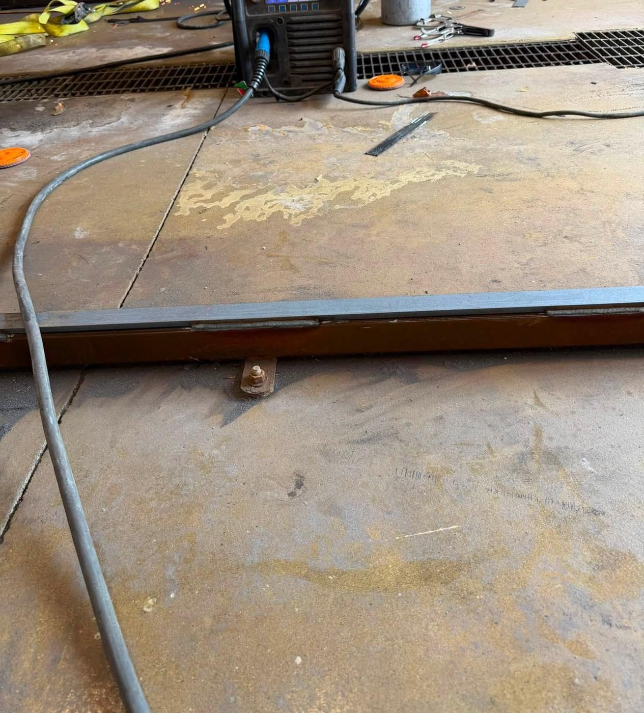 A welder set up on the shop floor beside a steel plate mid job