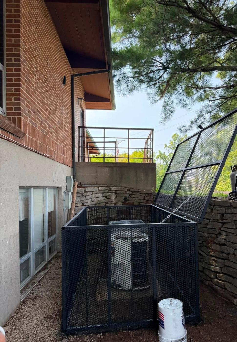 A steel security cage with a hinged lid built around an air conditioning condenser unit
