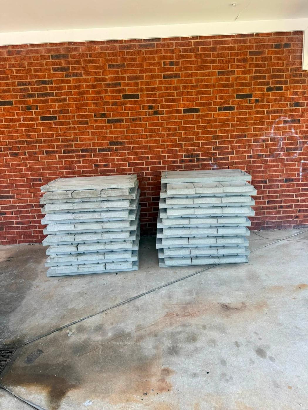 Two stacks of finished galvanized steel covers against a brick wall