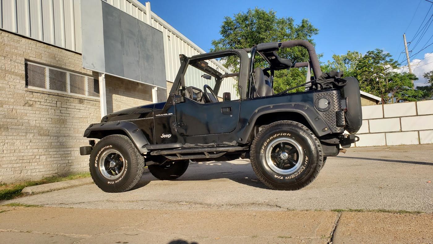 A black Jeep Wrangler side on at the shop, roll bar and rear mounted spare