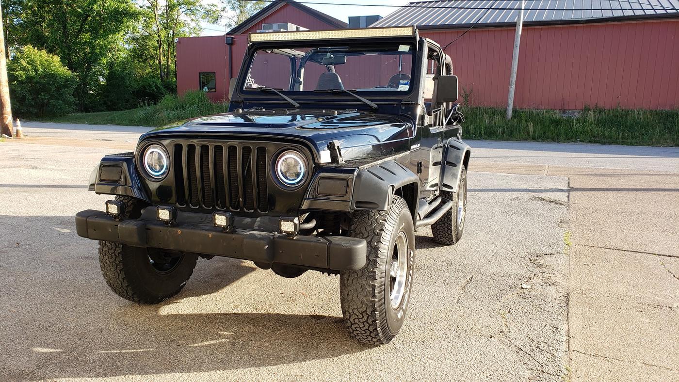 A black Jeep Wrangler with a tube front bumper parked outside the shop